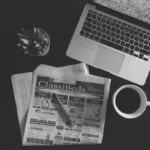 Publieditorial em Salvador: redação editorial com laptop, jornal e café em mesa de trabalho